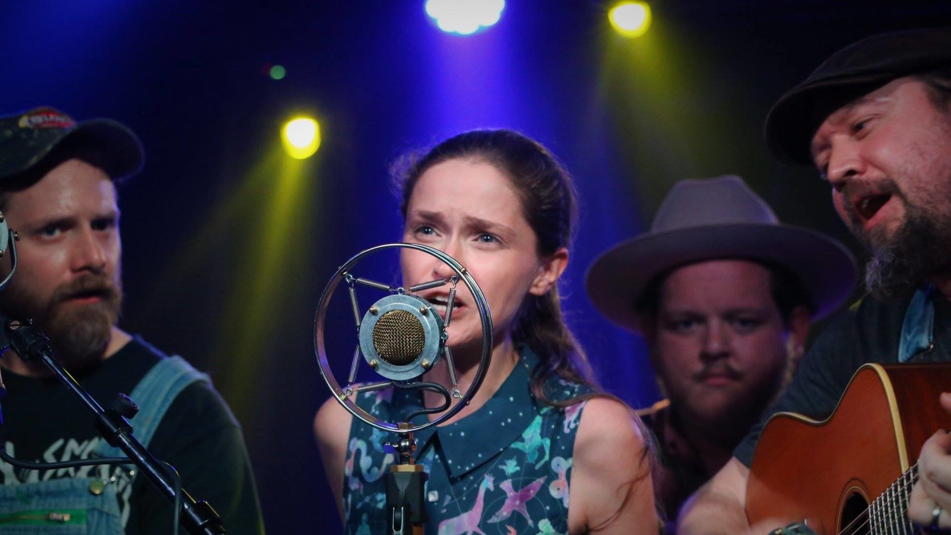 Jamie Lynn singing into a single mic with Trae and band members around her playing htier instruments.